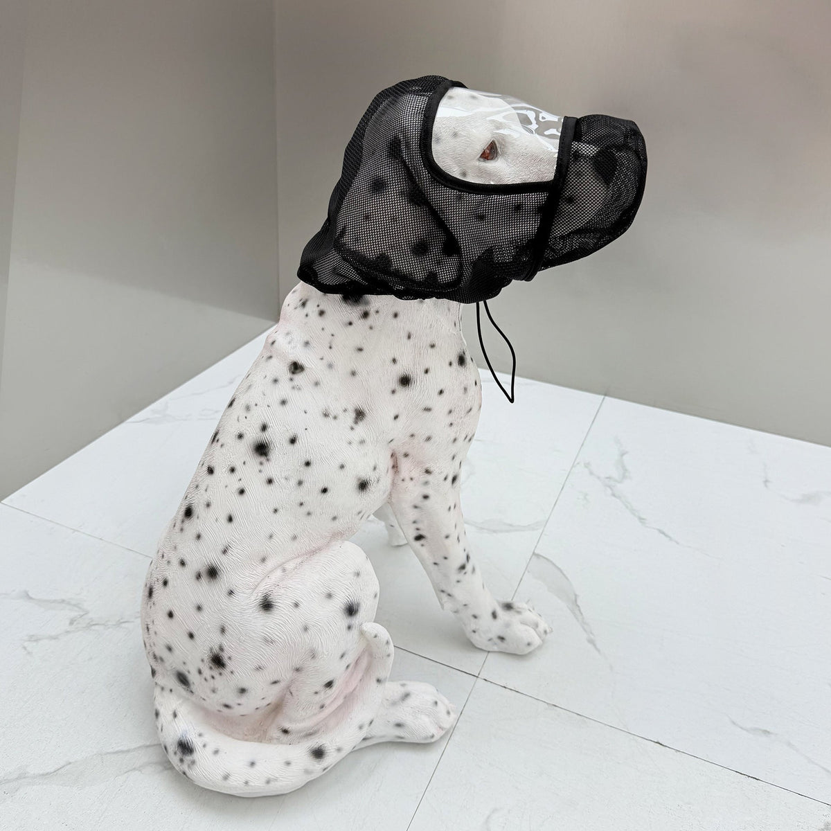 Dog wearing a black mesh muzzle on a white floor.