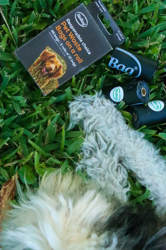 Pet waste bags and a brush on grass with a visible brand logo.