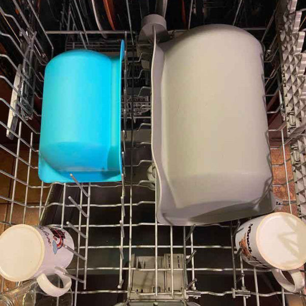 Dishwasher rack with a blue container, white bottle, and mugs.
